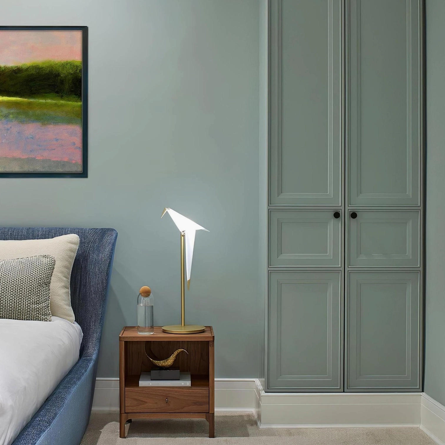 Origami crane table lamp on wooden surface in plant-filled indoor nook with brass pole and white shade
