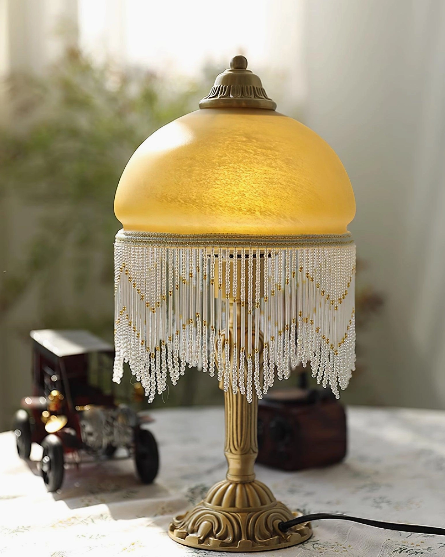 Ornate brass base of vintage tassel table lamp with beaded tassel decoration and frosted amber glass dome
