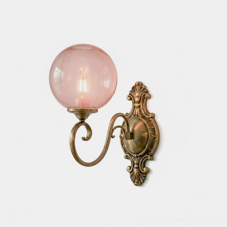 Ornate brass wall sconce with pink hand-blown glass globe, vintage baroque backplate design, studio front view