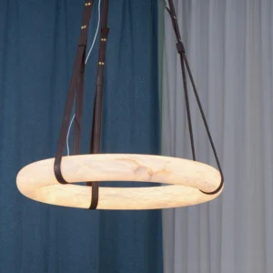 Oslo modern pendant light installed in home with dark brown leather straps and illuminated alabaster shade, low side angle view