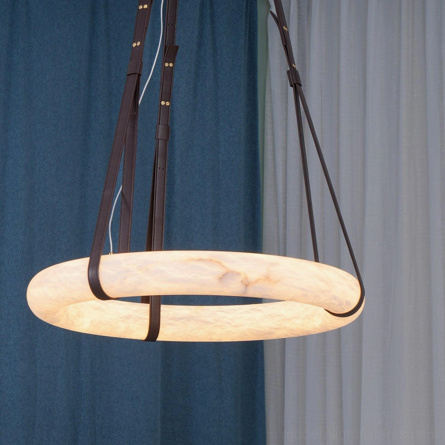 Oslo modern pendant light installed in home with dark brown leather straps and illuminated alabaster shade, low side angle view