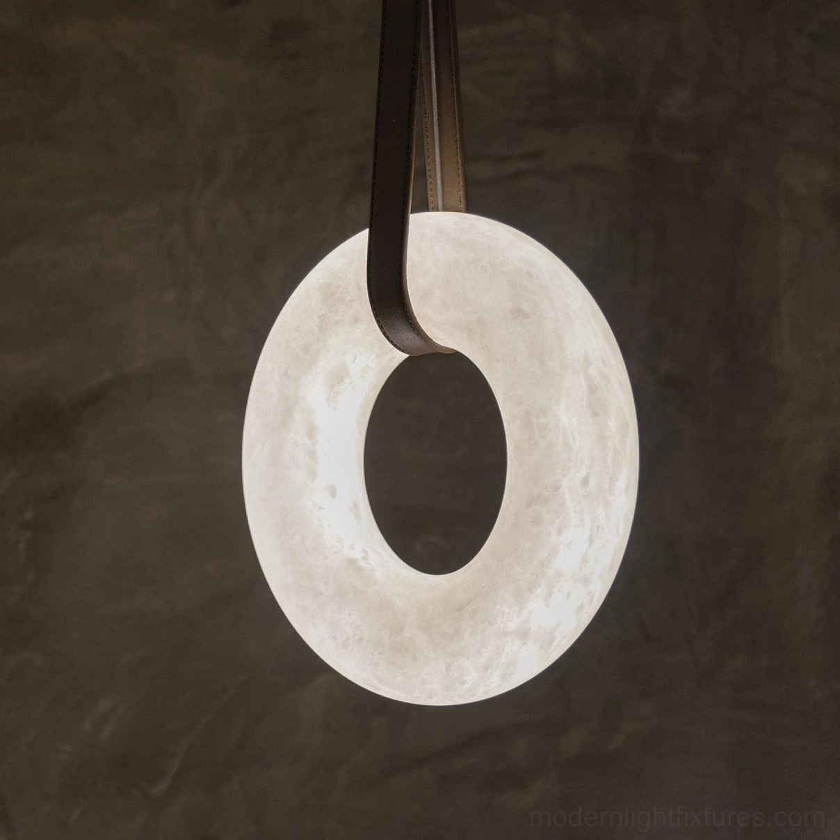 Close-up detail of matte alabaster ring shade with natural stone texture and warm brown leather suspension strap against textured wall