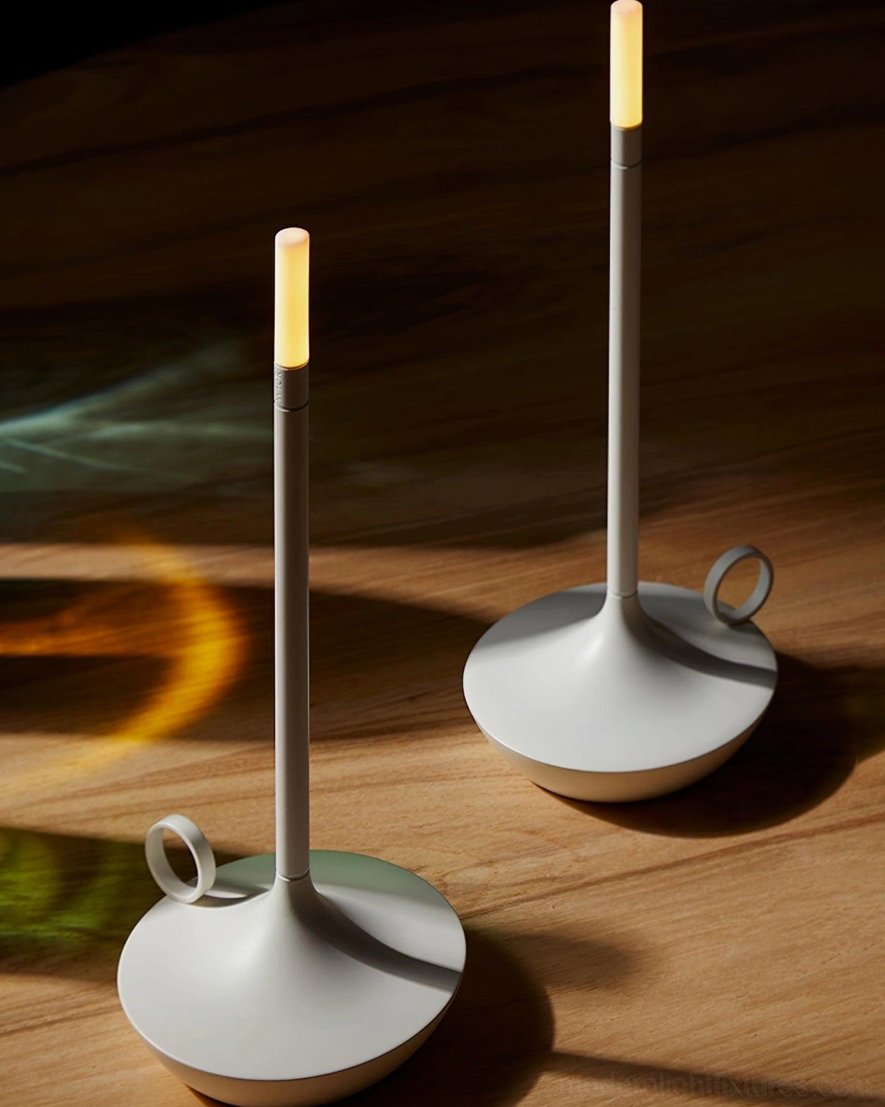 Pair of minimalist LED candle lamps in neutral finishes positioned on wooden desktop, low angle view showing compact design