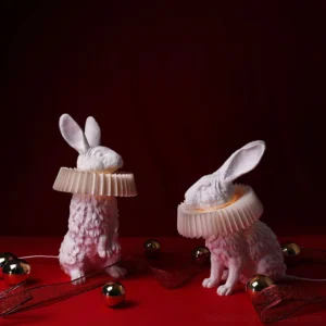 Pair of white rabbit resin table lamps with pleated shades displayed on festive holiday tabletop with ornaments and decorations