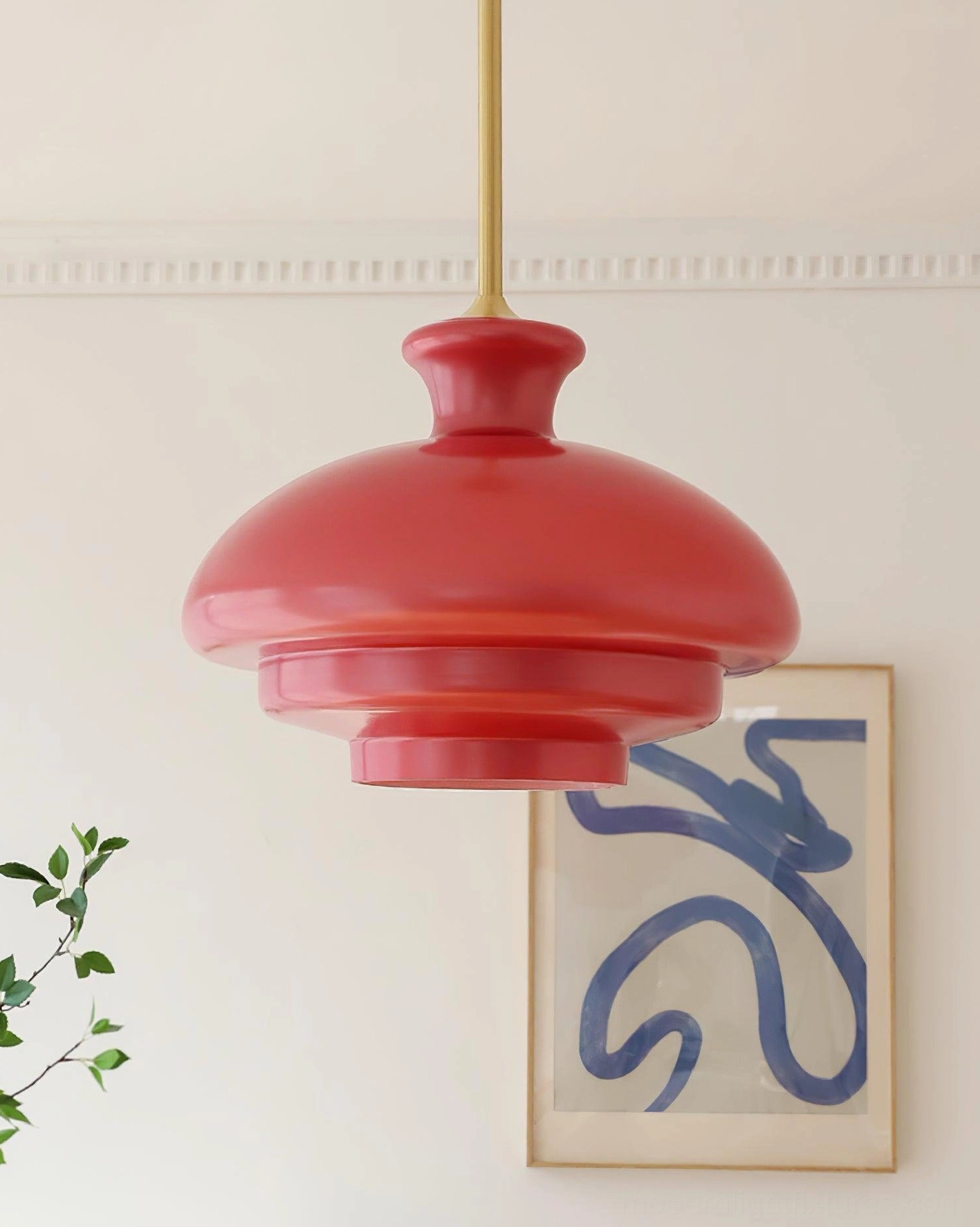 Paolina deep red tiered glass pendant light suspended in modern home with abstract wall art and green foliage, side three-quarter view