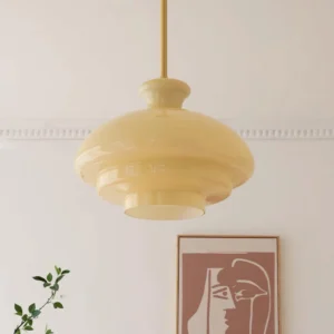 Paolina tiered glass pendant lamp in warm yellow, suspended in residential home with crown moulding and plant decor, three-quarter angle