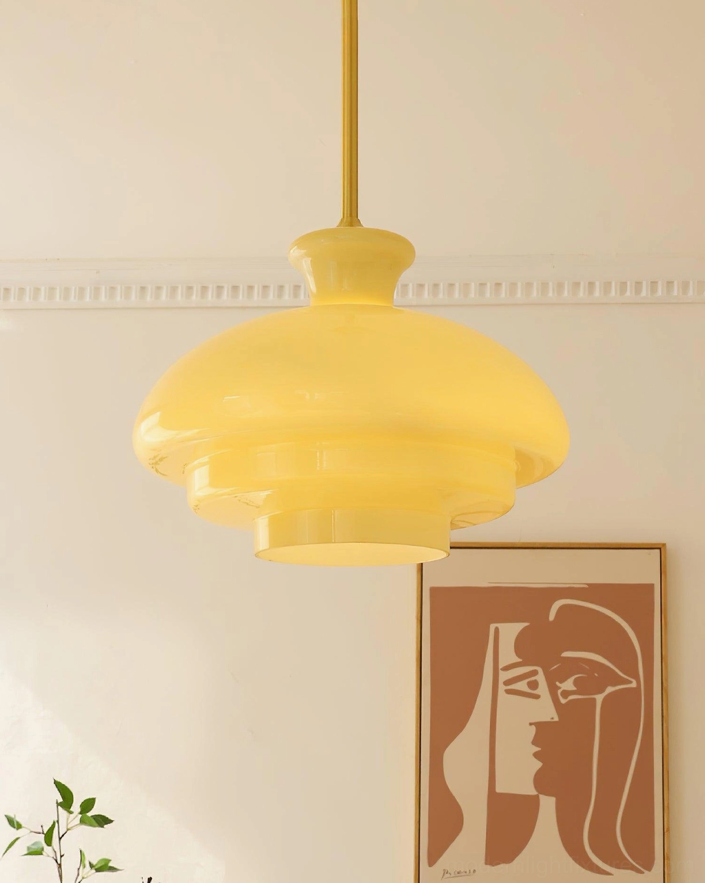 Paolina tiered glass pendant light in warm yellow shade with brass hanging rod, overhead perspective in home setting with wall art