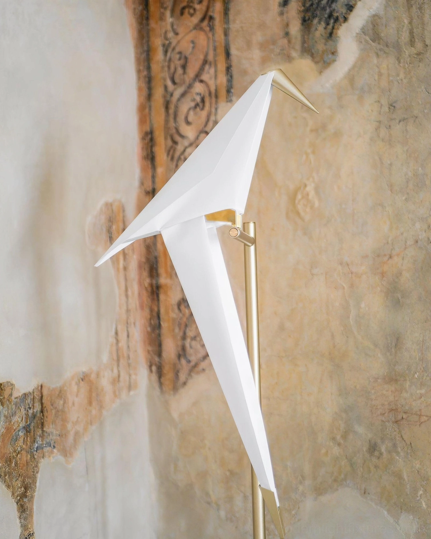 Close-up detail of polished brass metal stem and white origami bird shade, low-angle view