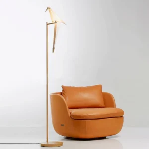 Modern paper crane floor lamp in living room setting with leather armchair, three-quarter angle view
