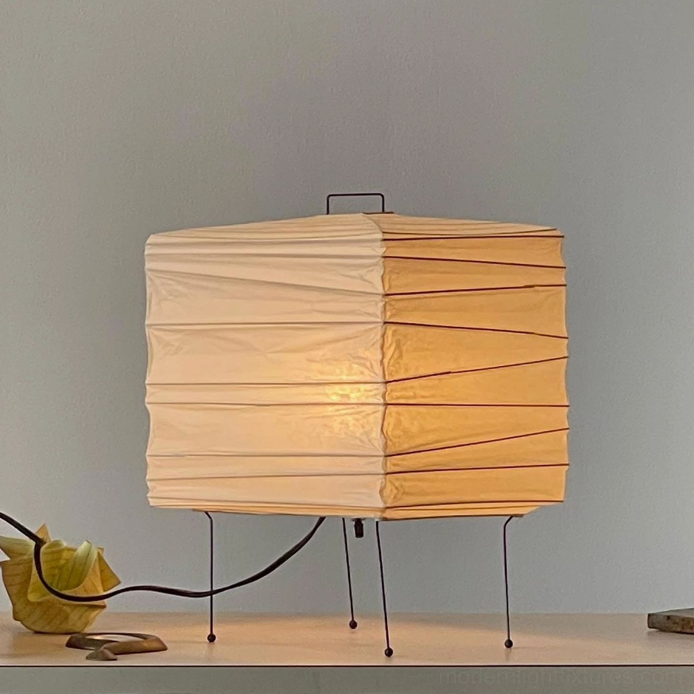 Black metal frame paper cube table lamp with warm ambient lighting in side angle view