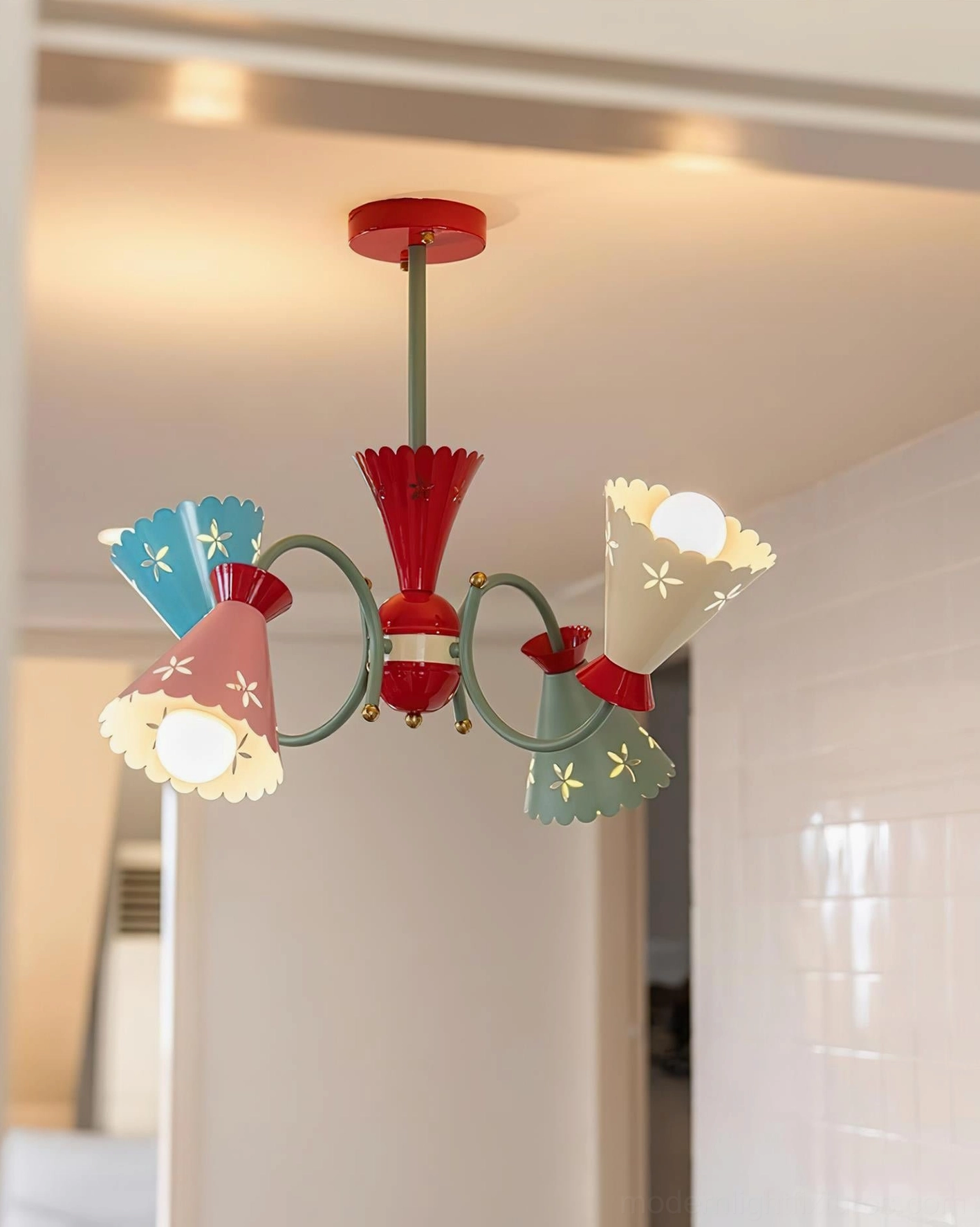 Three-quarter front view of illuminated pastel chandelier in tiled room showing reversed shade color order and vintage playful aesthetic