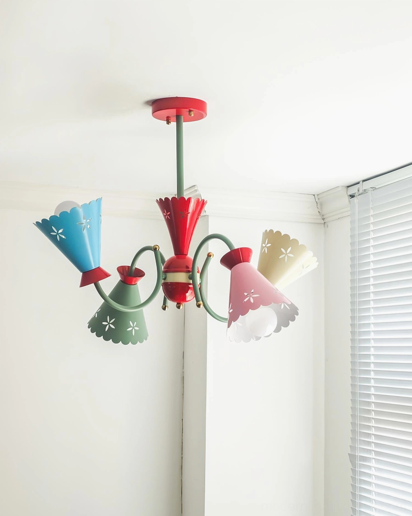 Three-quarter side view of pastel 5-arm chandelier near window blinds demonstrating compact hanging design and playful multicolor scheme