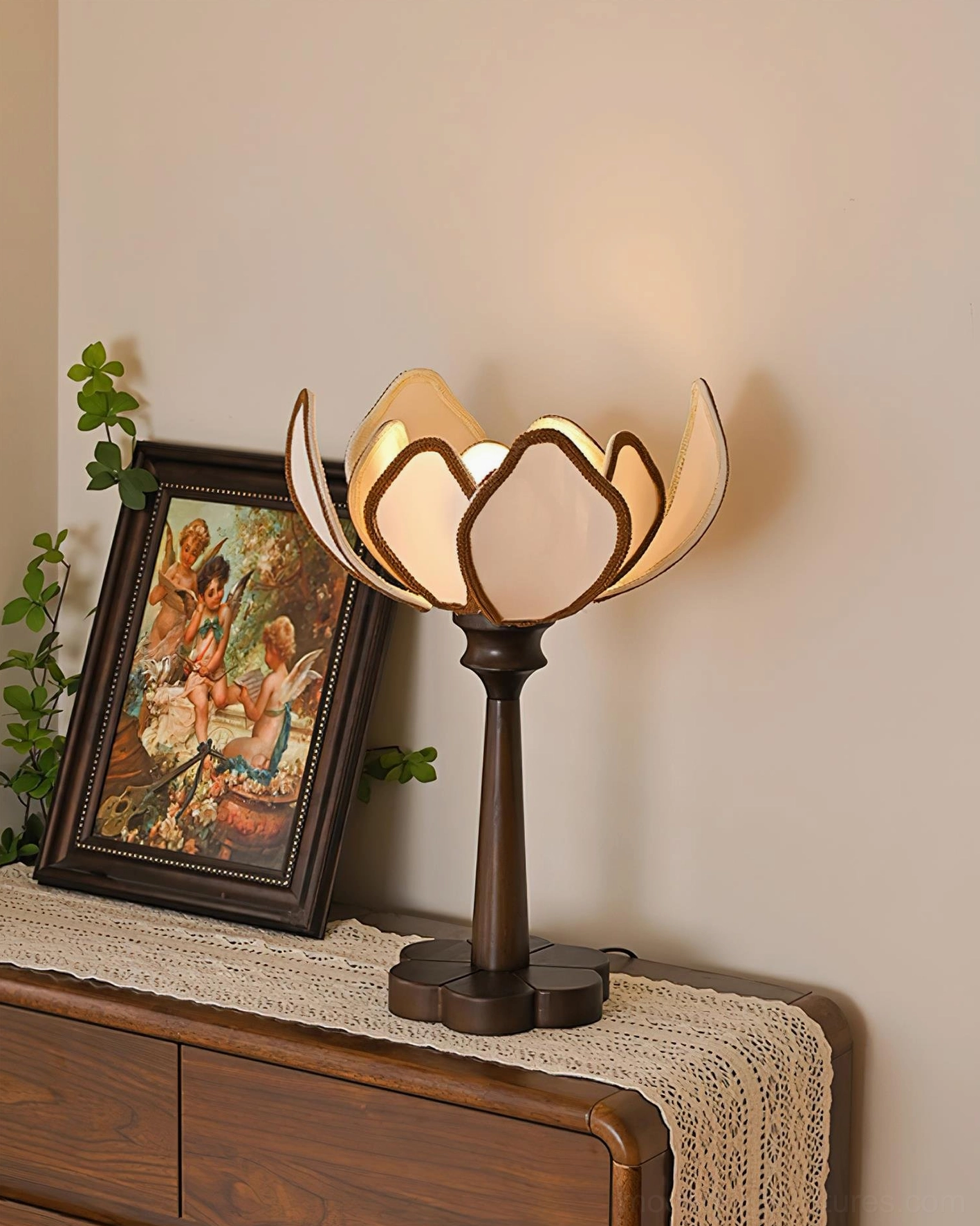 Rear view of glowing Pauline table lamp on antique dresser with trailing greenery and vintage painting decoration