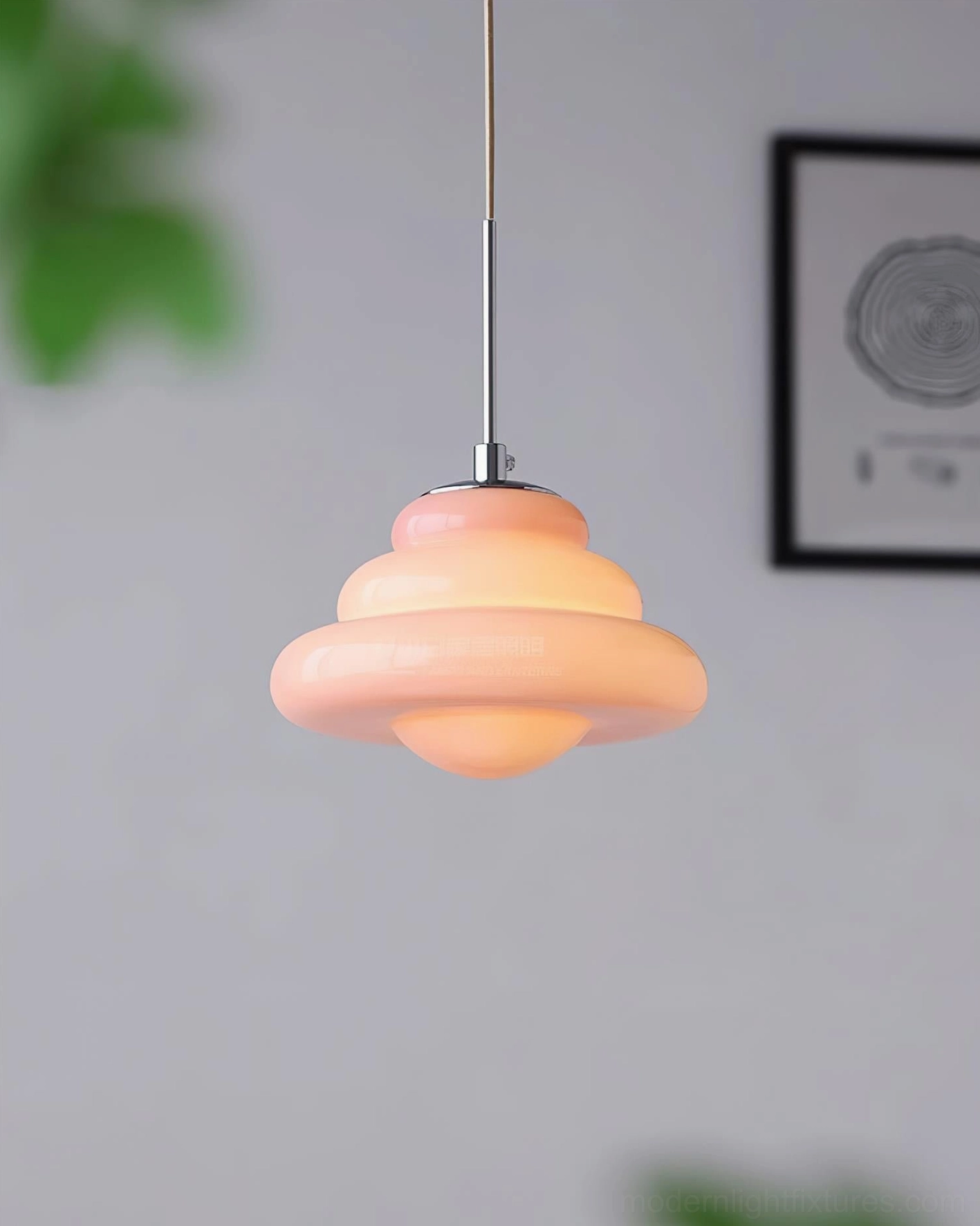 Light peach pink tiered pendant light hanging in cozy minimalist home with wall art and plants