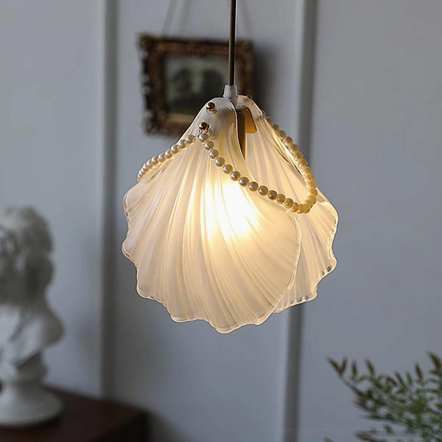 Close-up detail of frosted glass shell-shaped pendant lamp with pearl beading and warm light