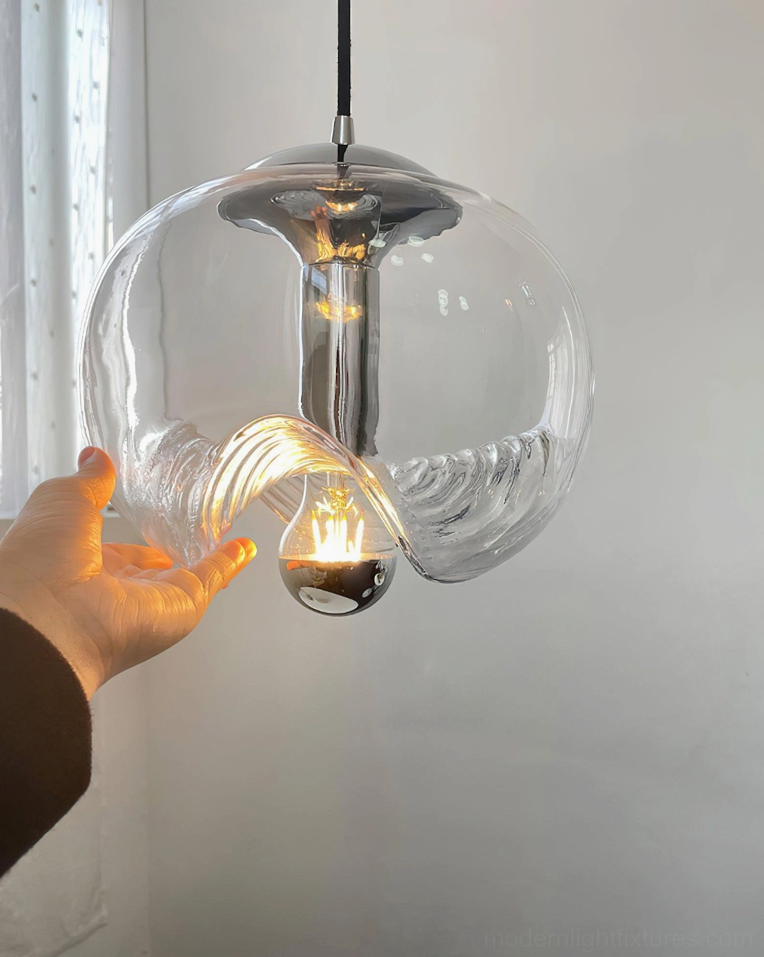 Modern wave glass pendant lamp hand-held close-up view showing exposed bulb detail and polished metal hardware construction