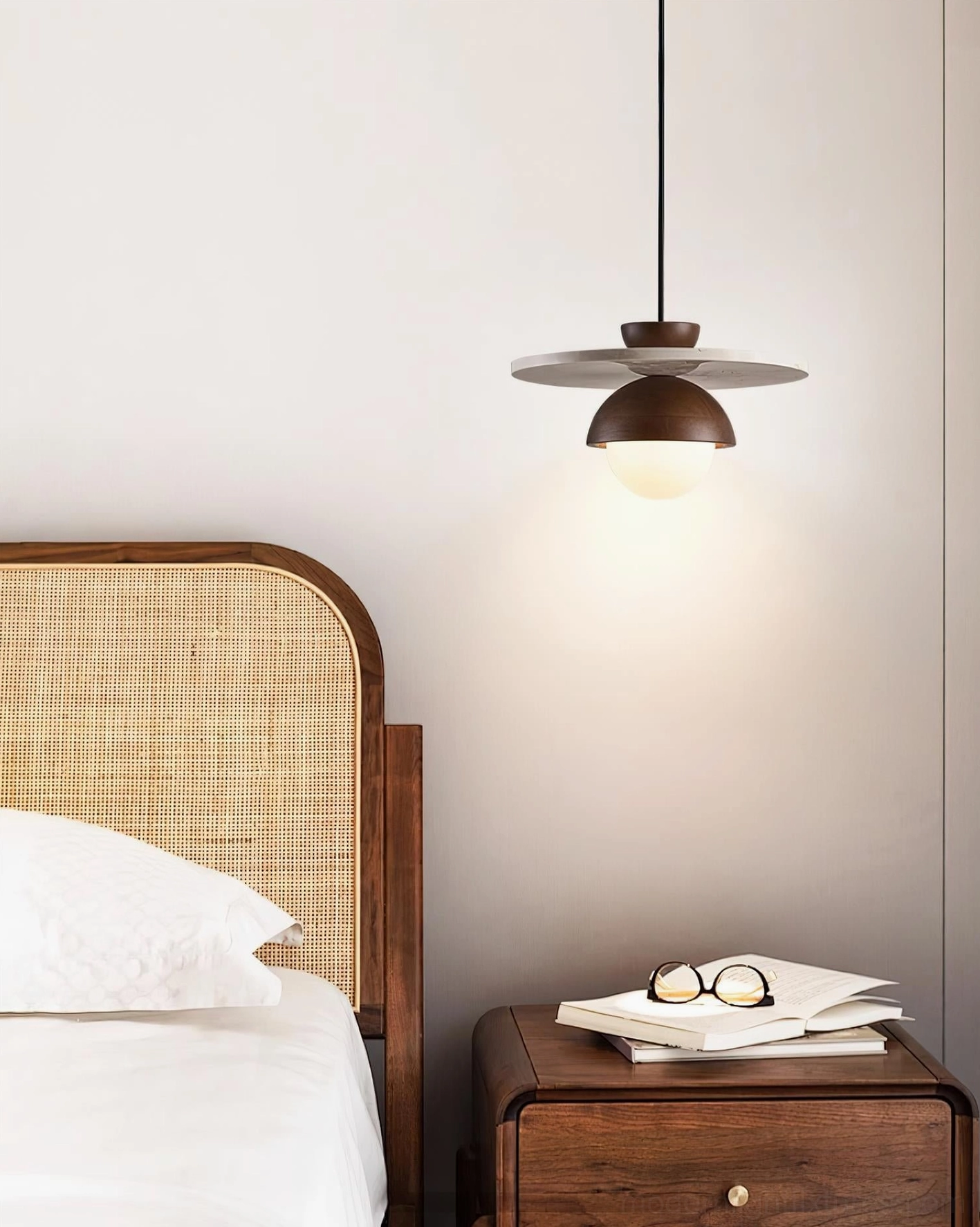 Contemporary pendant light fixture above wooden bedside table with reading materials and neutral decor