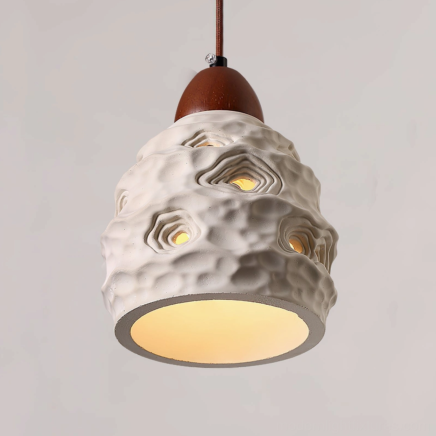 Ceramic pendant light installation showing warm light diffusion through perforations creating ambient shadow patterns
