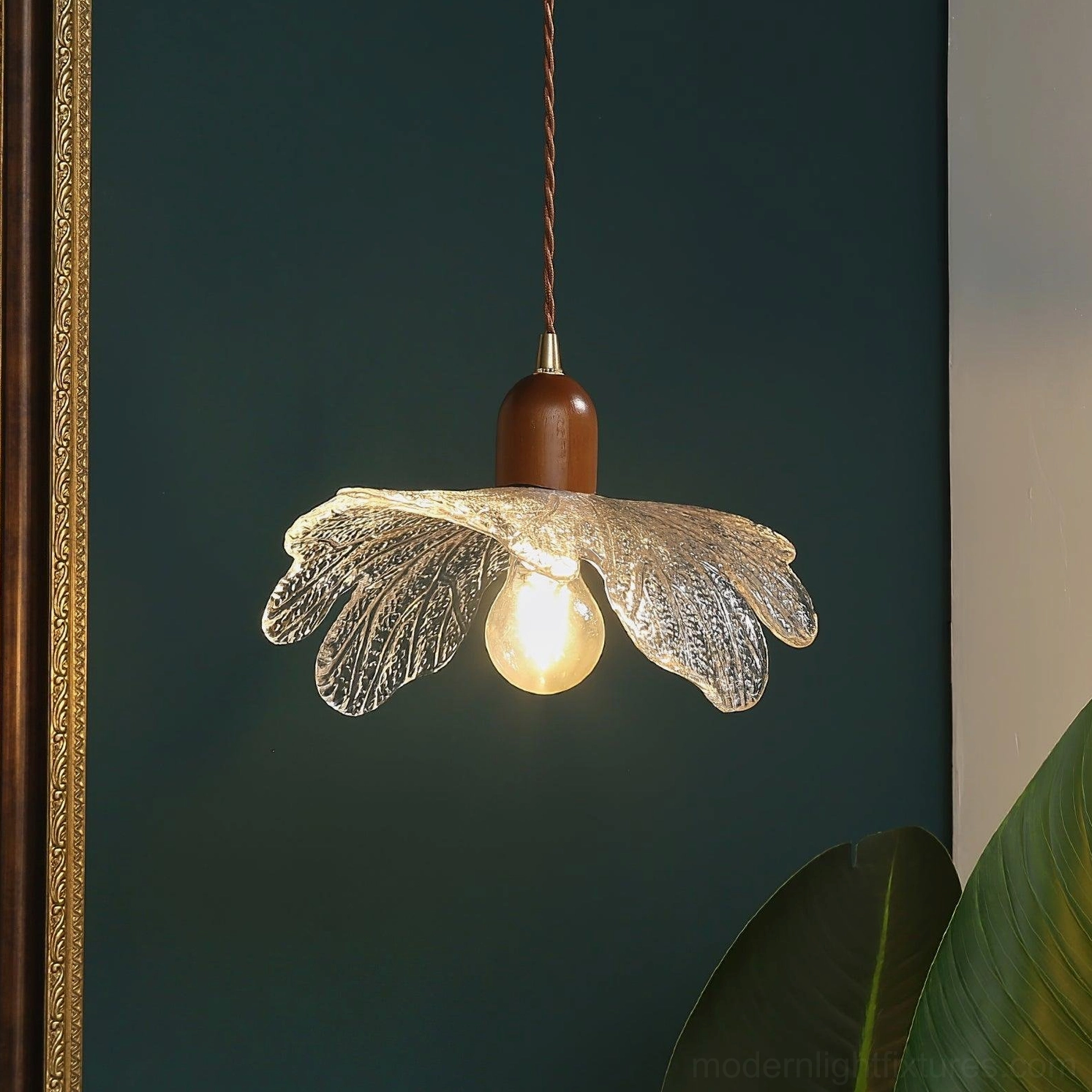 Modern floral pendant light installed above dark green wall with gold frame, warm ambient lighting