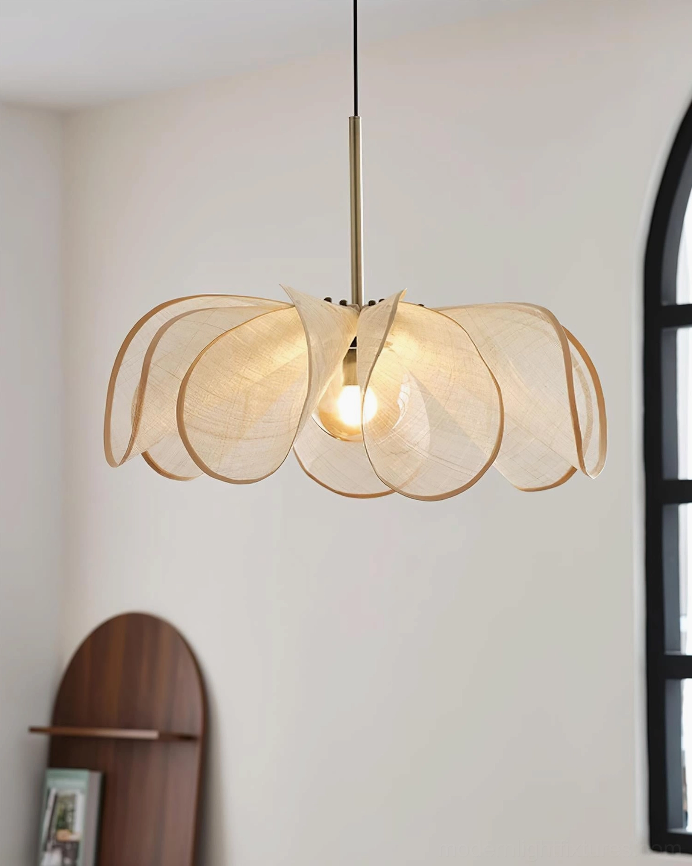Natural jute petal pendant lamp with brass suspension rod and warm ambient lighting in minimalist home with black arch window