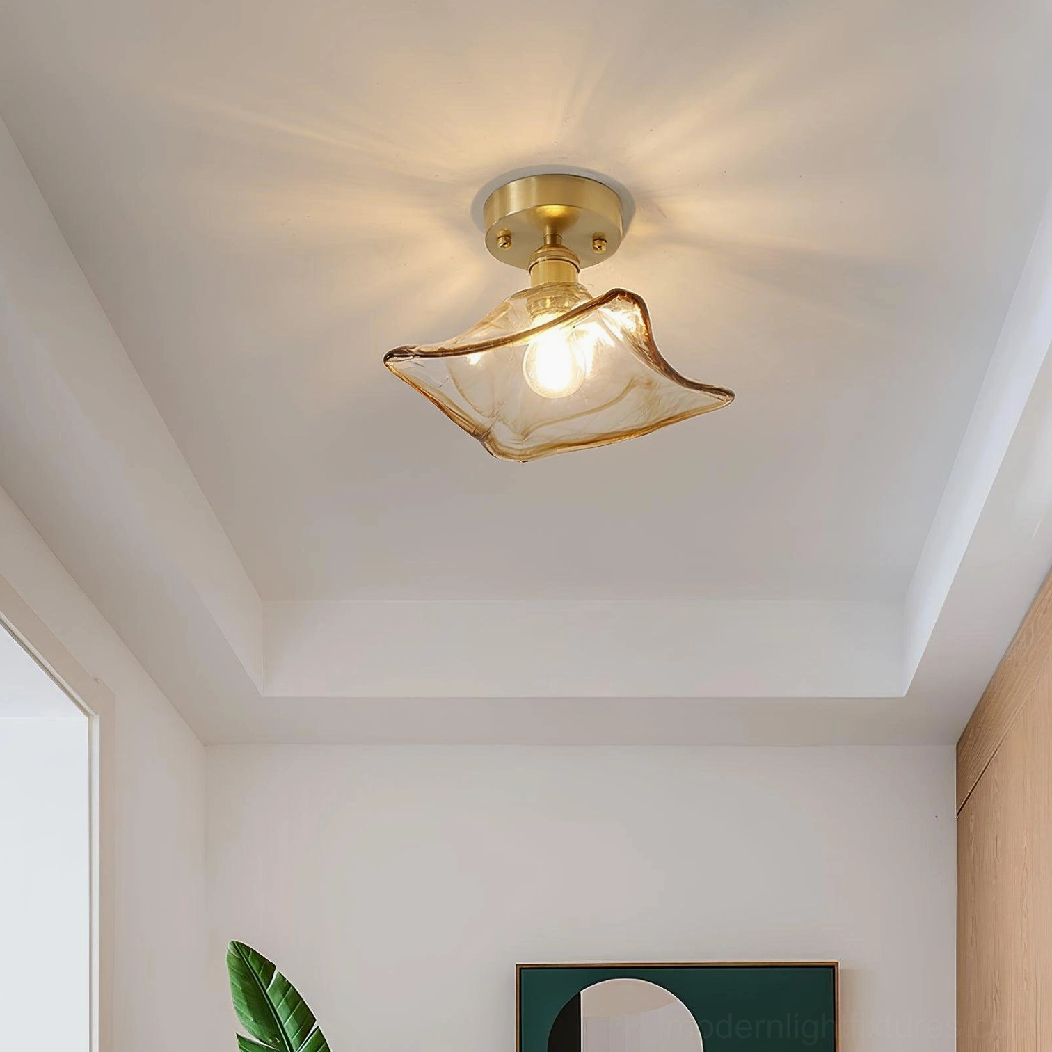 Petal-shaped amber glass semi-flush ceiling light with brass gold base mounted in minimalist entryway with white walls