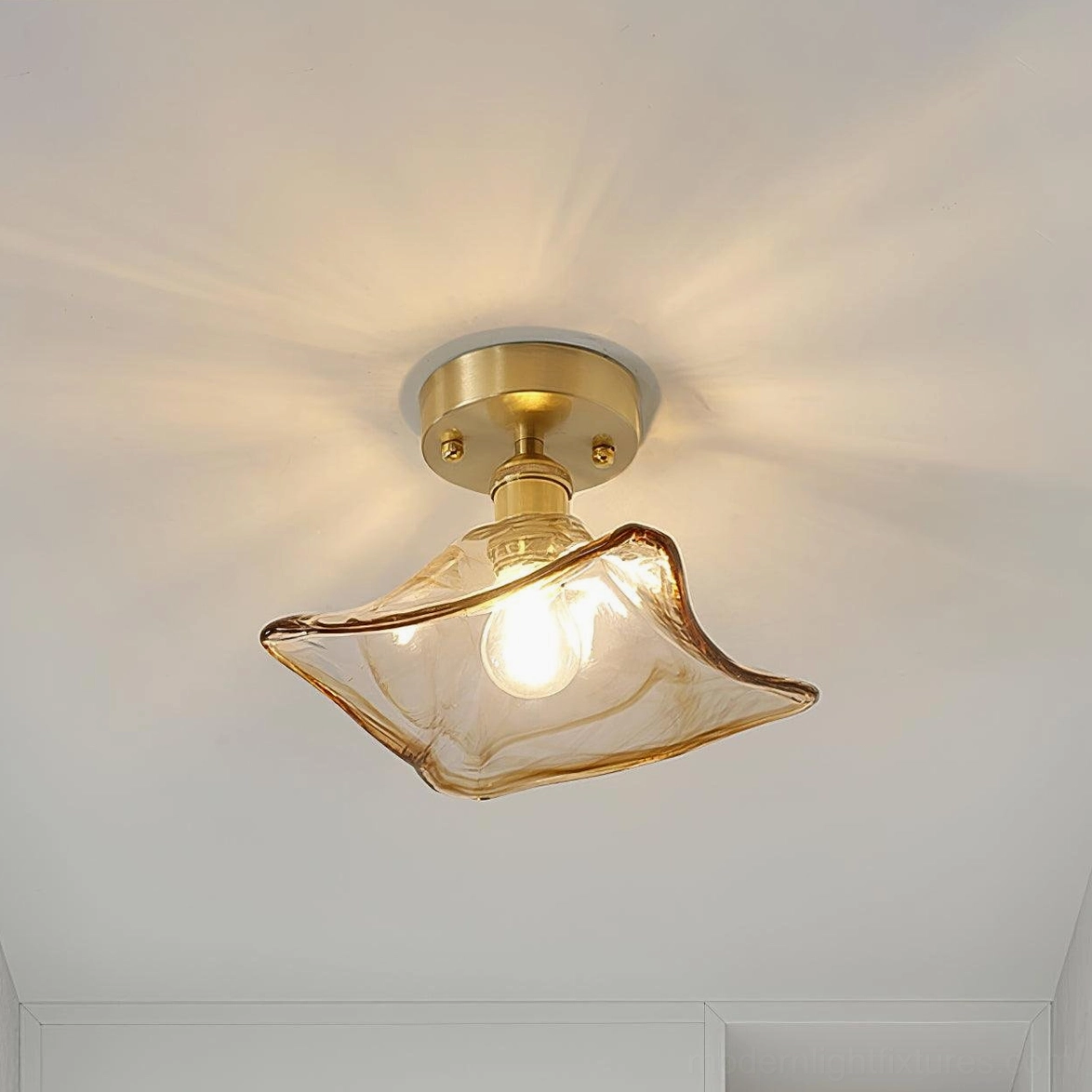 Petal-shaped amber glass flush mount ceiling light with brass gold base mounted in minimalist indoor corridor