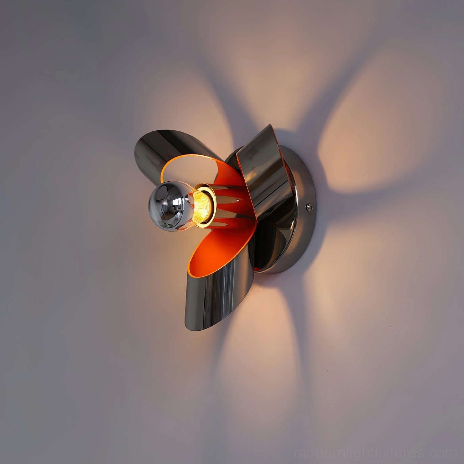 Petala wall sconce with lit warm bulb and dark metallic finish creating distinct shadow patterns, front three-quarter view on wall with framed artwork