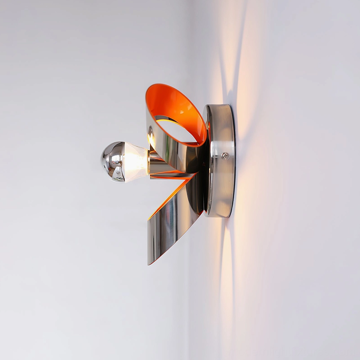 Petala wall sconce side profile view with exposed bulb, angled metallic petals, and warm lighting effect on white wall corner