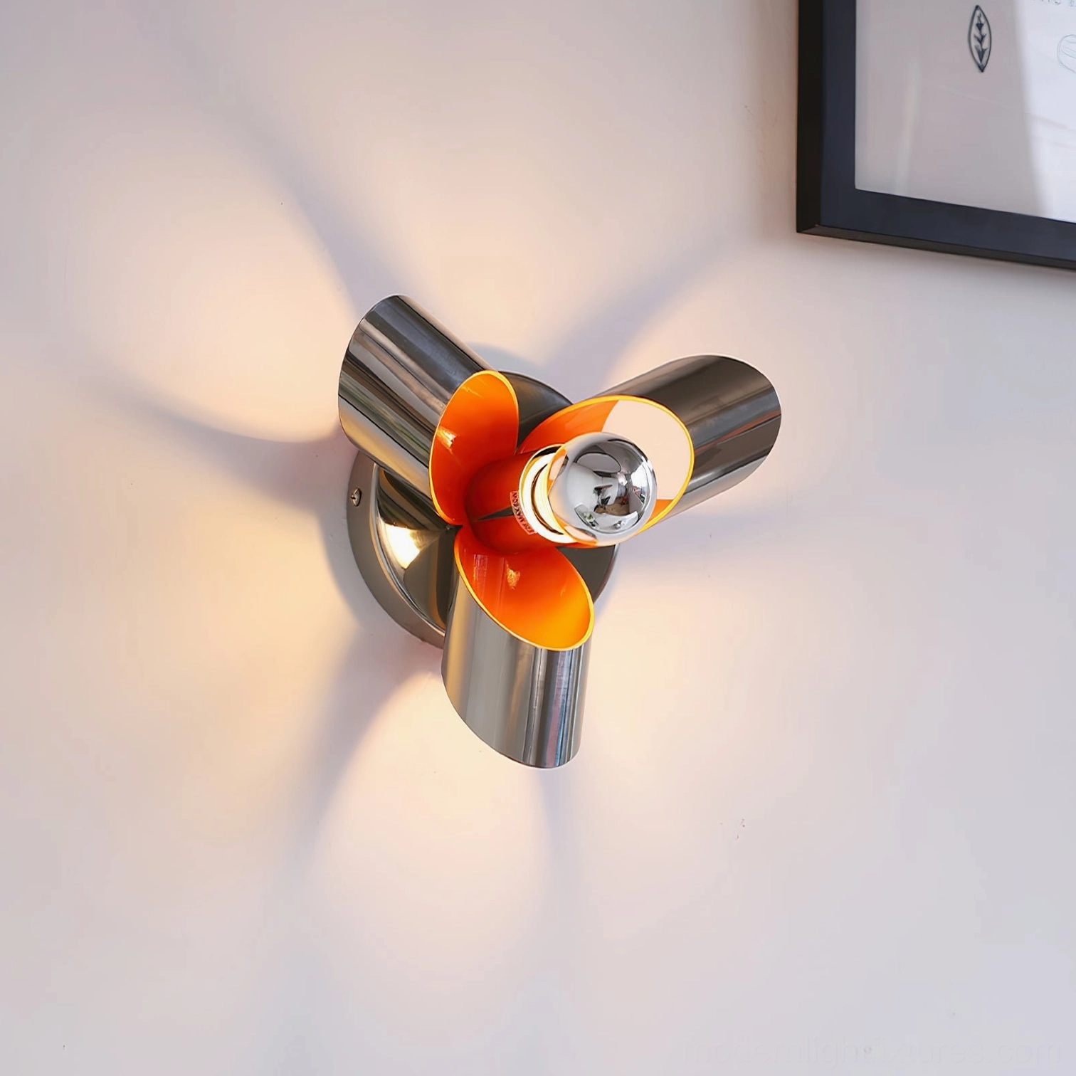 Illuminated Petala wall sconce casting warm light and shadows, side three-quarter angle showing polished metallic finish against indoor wall