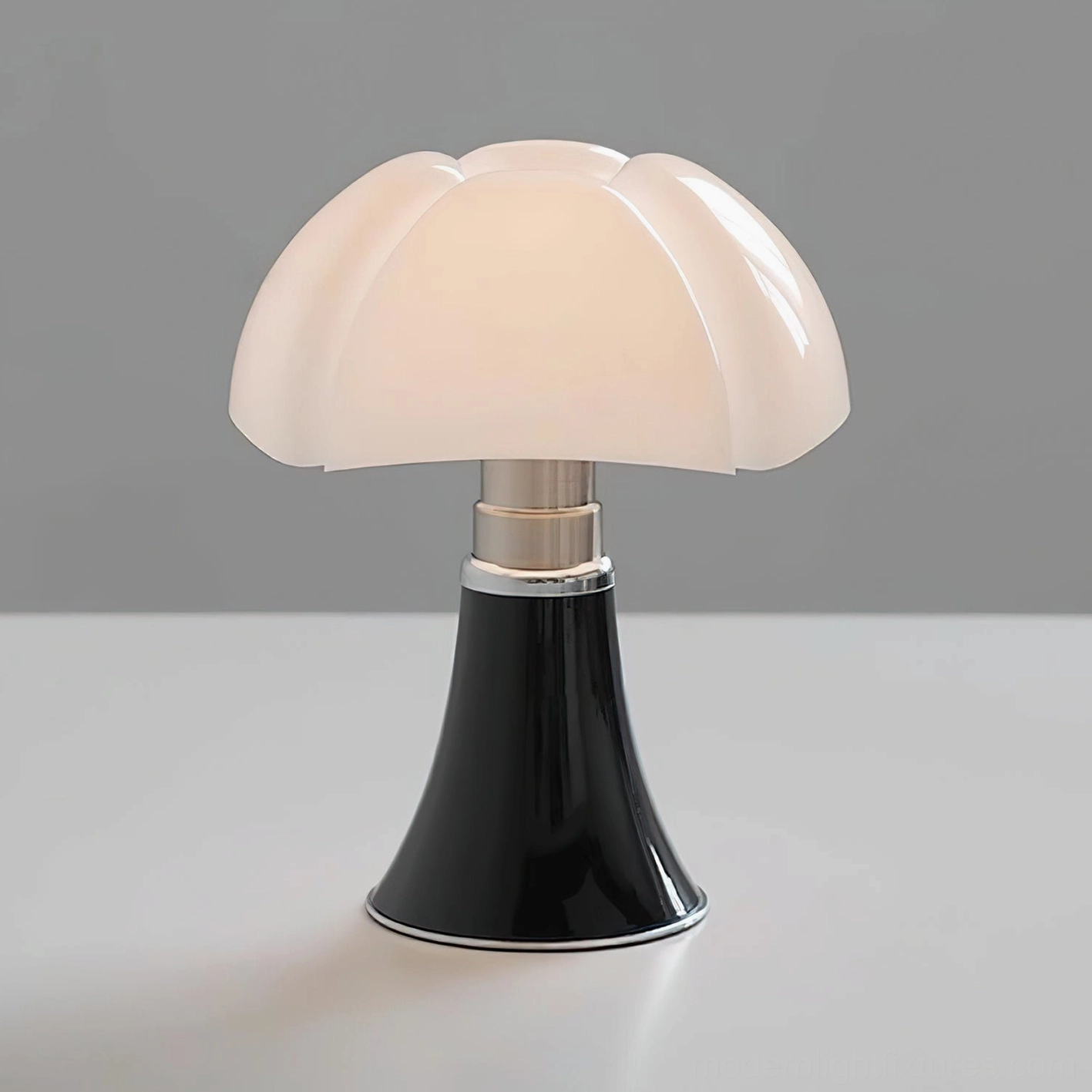 Petalica adjustable table lamp three-quarter view showing flared black base with silver trim and white acrylic petal shade on gray tabletop