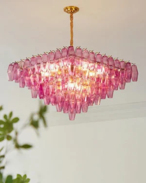 Modern Petralyn pyramid chandelier illuminated in home interior with green foliage three-quarter angle view