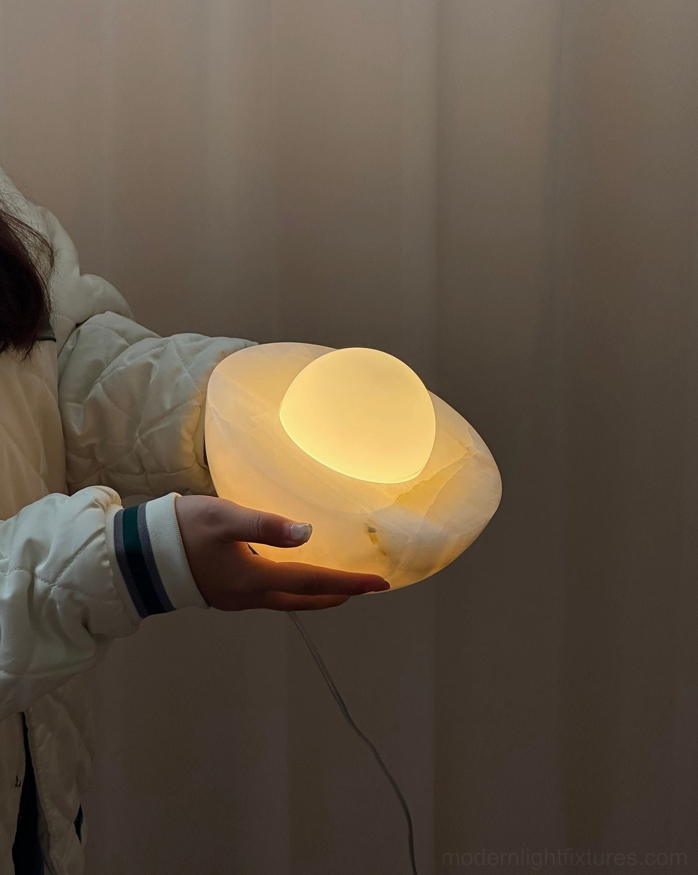 Illuminated Piccola onyx marble table lamp handheld view with warm light glow and natural stone grain pattern