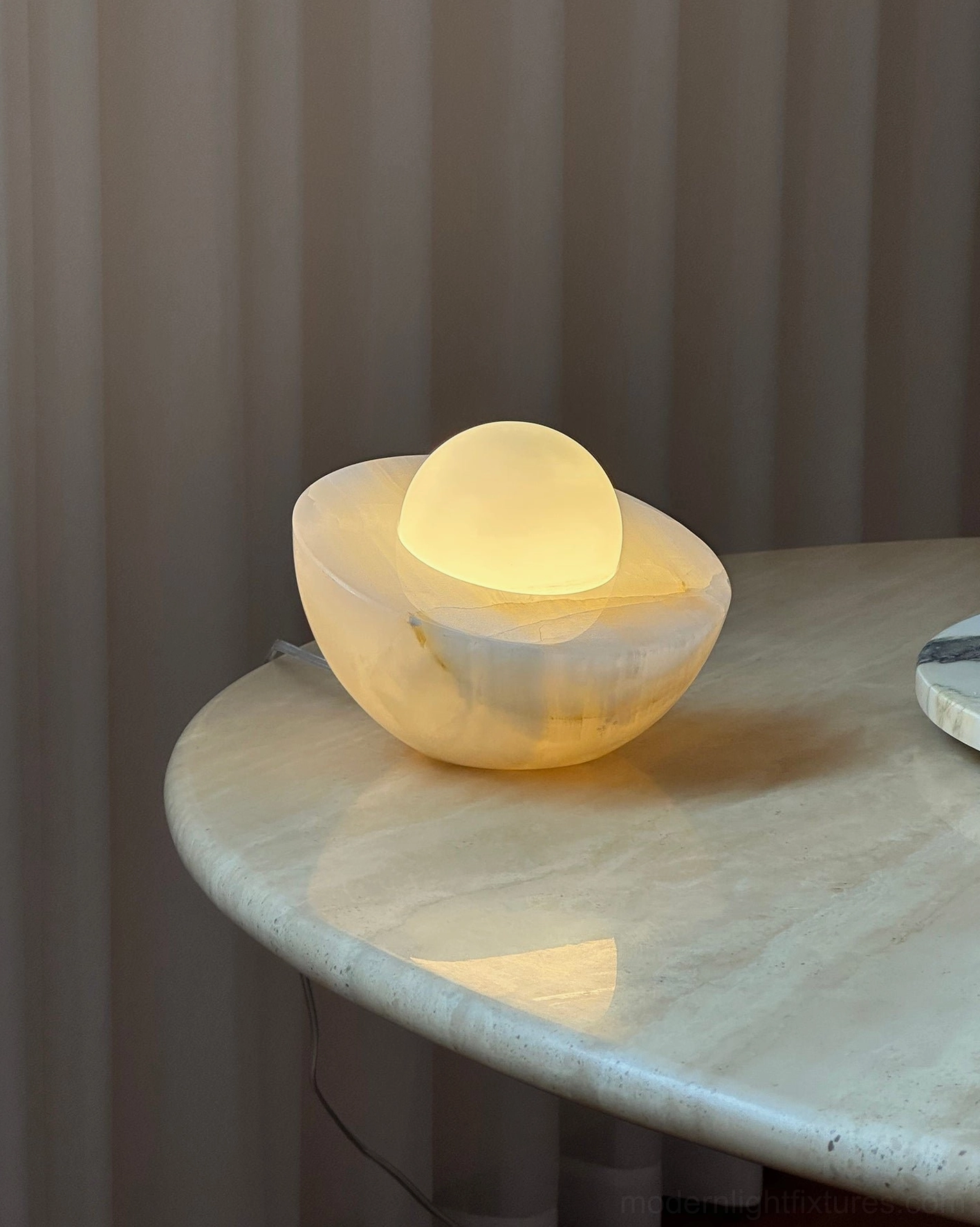 Lit Piccola onyx table lamp three-quarter view warm ambient glow home dining reflective marble surface
