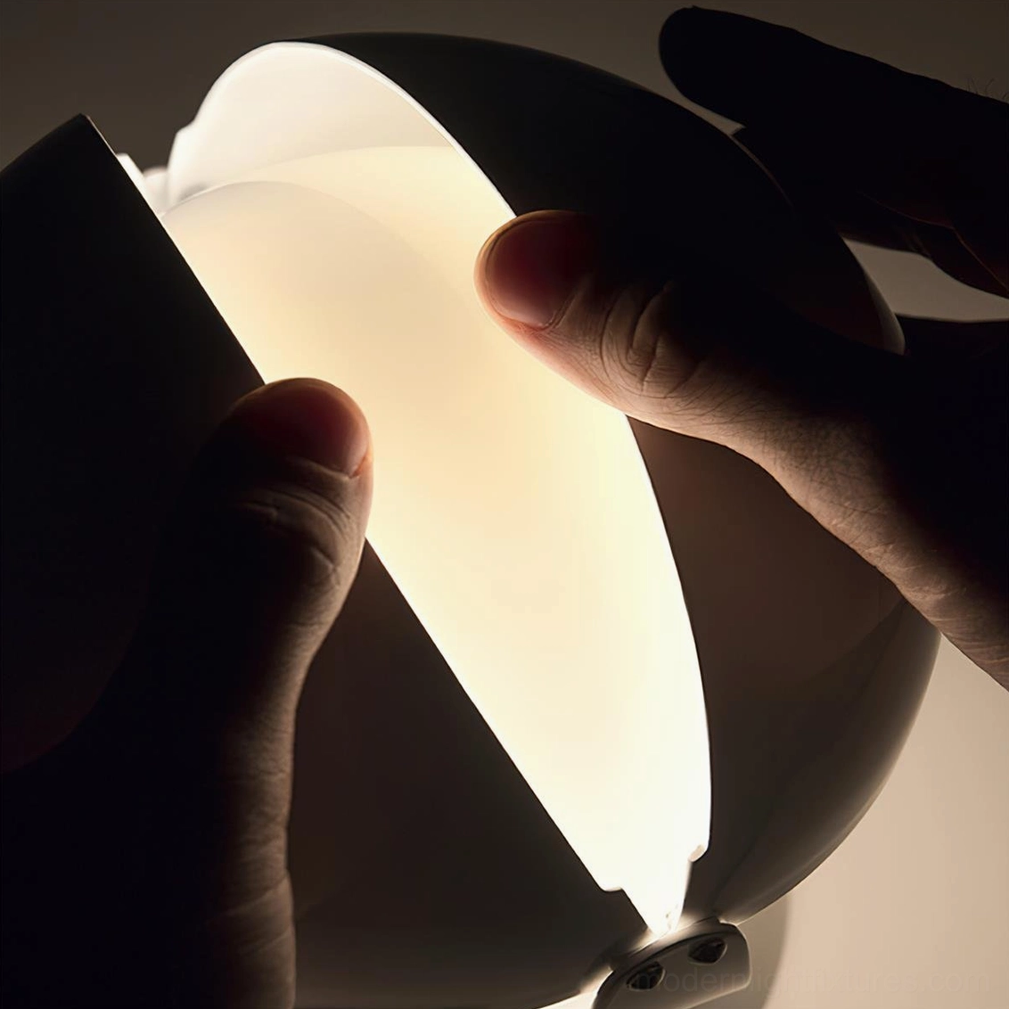 Close-up side view of Pileino table lamp with hand adjusting the pivoting split shade revealing interior light