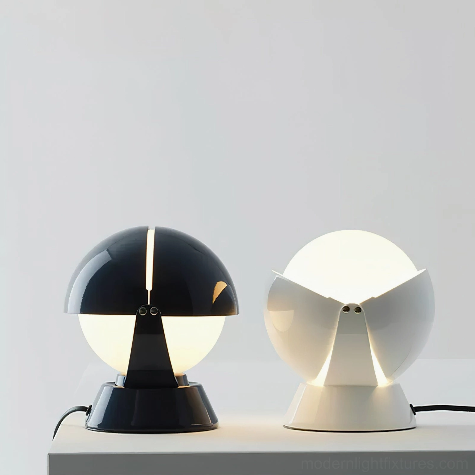 Two Pileino table lamps in black and white colorways illuminated with warm light on studio display shelf