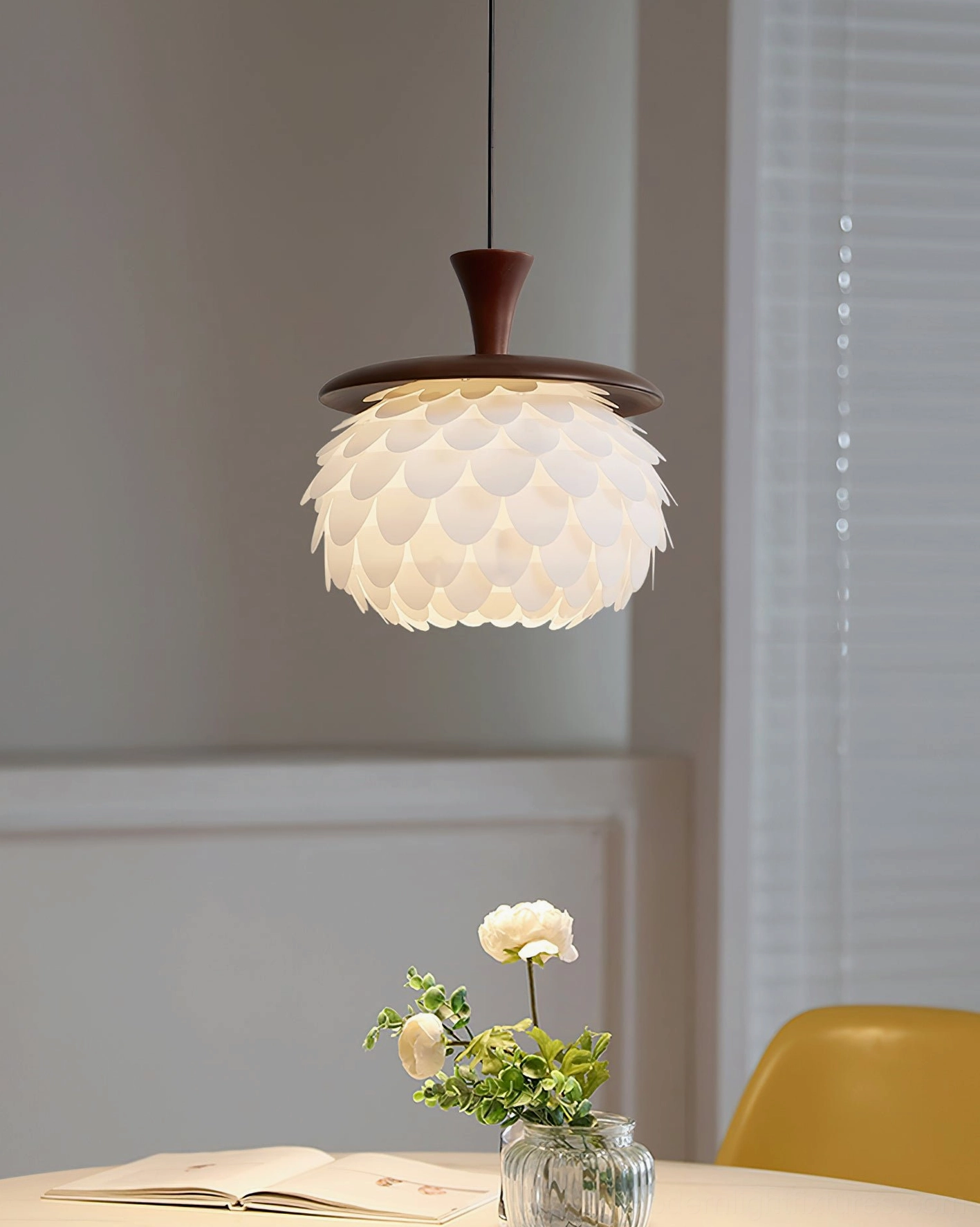 Modern pendant light fixture above casual home dining area with yellow chairs and flower centerpiece - creating intimate ambient lighting