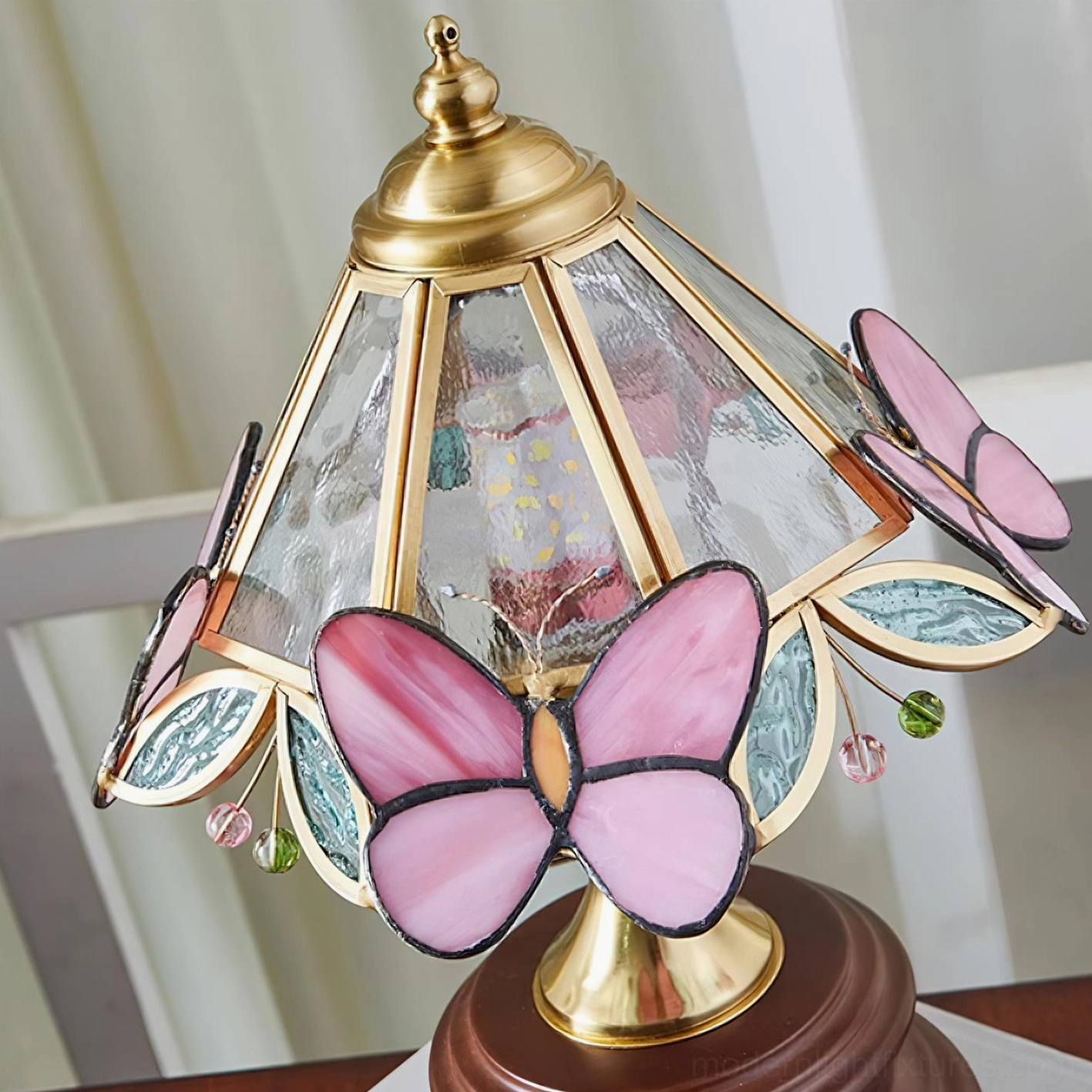 Close-up side view of pink stained glass butterfly lamp shade with decorative bead and brass trim details