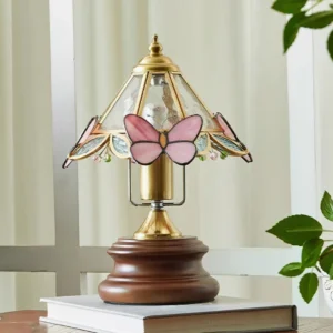 Vintage Tiffany-style pink butterfly table lamp displayed on wooden side table with stacked books and green plants