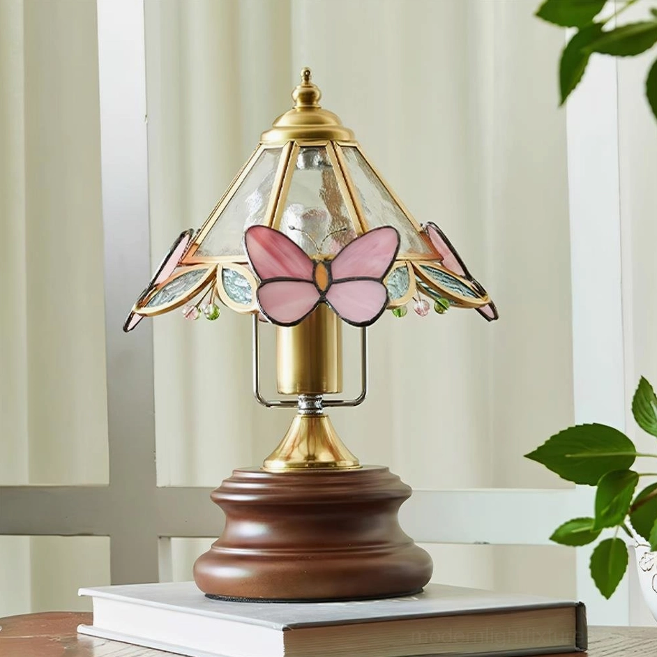 Vintage Tiffany-style pink butterfly table lamp displayed on wooden side table with stacked books and green plants