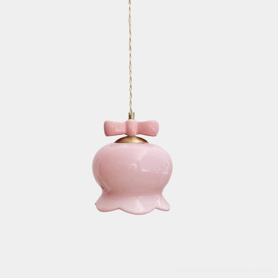 Pink ceramic bellflower pendant light with bow detail, hanging against white studio background