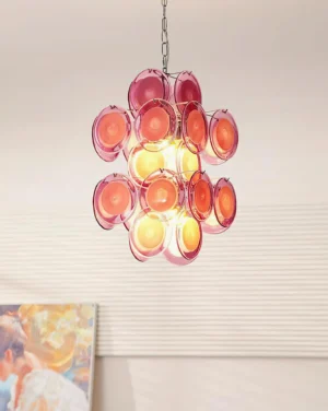 Illuminated pink glass disc pendant chandelier hanging in interior space with textured wall