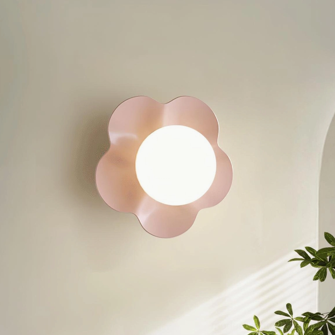 Pink Fleur wall sconce mounted on beige wall with green foliage - sculptural resin flower lamp with frosted glass diffuser glowing warmly