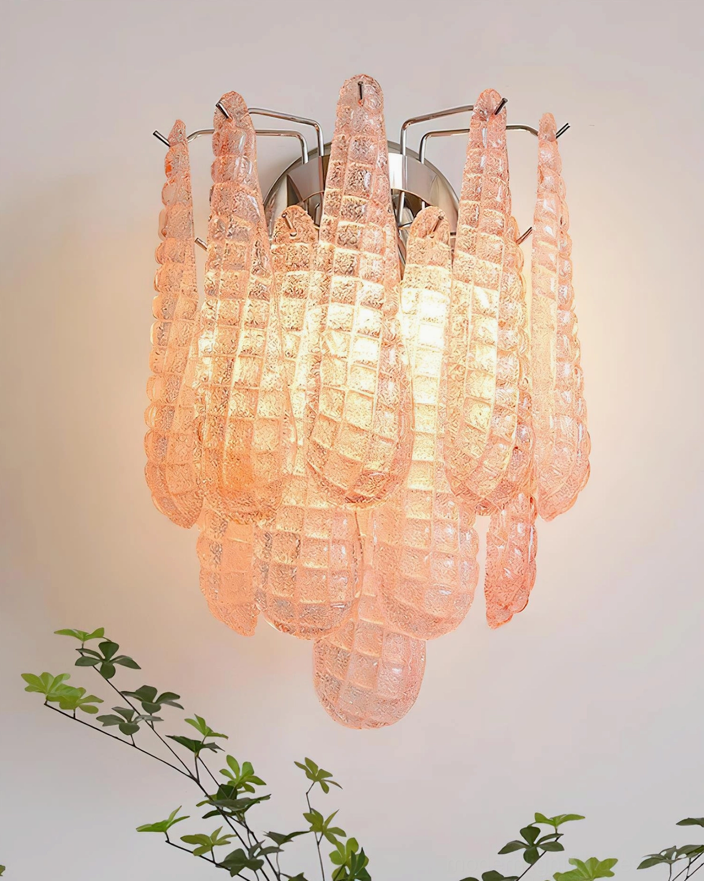 Illuminated pink glass wall sconce installed in modern home interior with green plant decor
