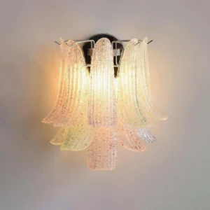 Illuminated pink petal glass wall lamp glowing warmly against beige wall, showing light diffusion and layered glass petals