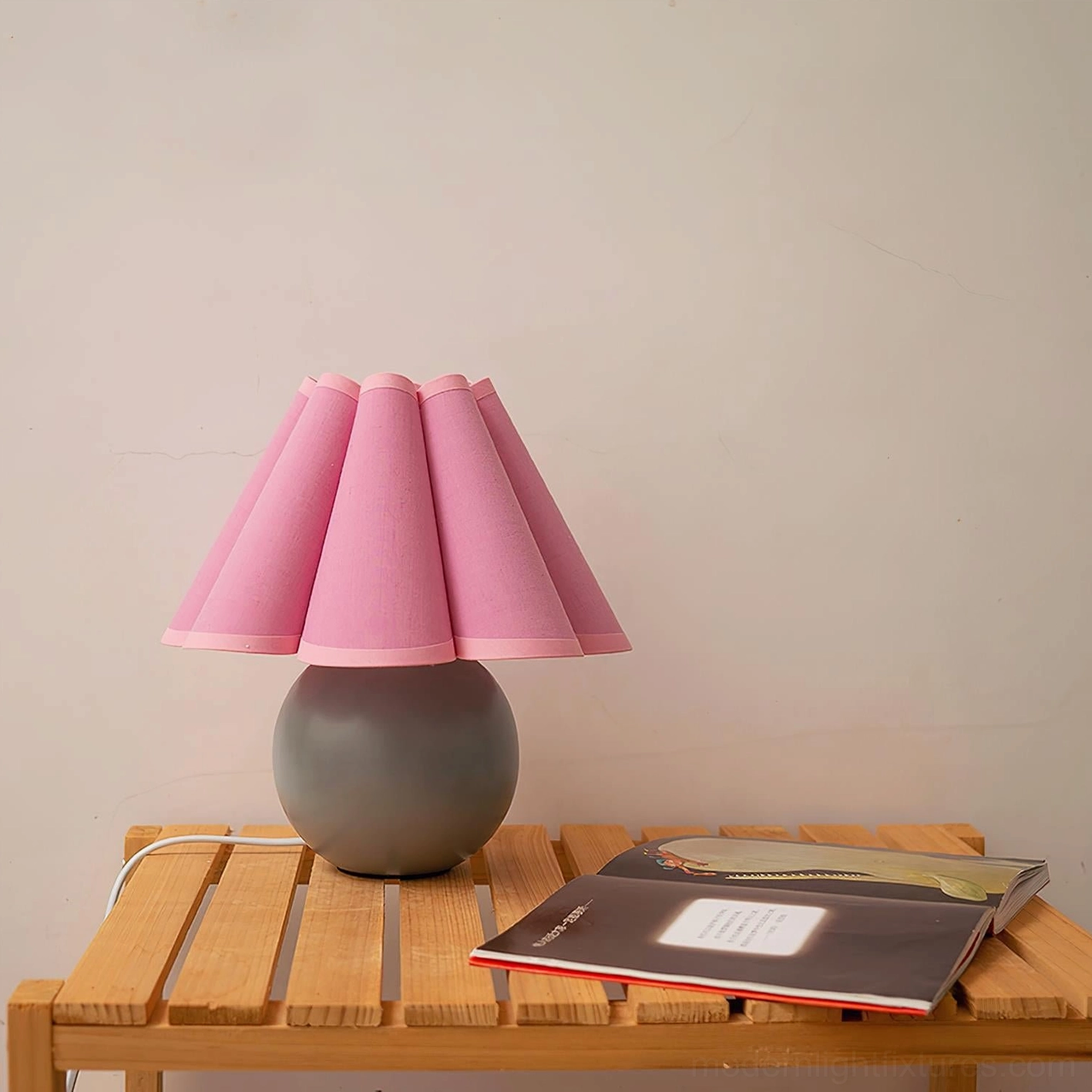 Pink pleated fabric shade table lamp with gray ceramic spherical base on wooden furniture in contemporary interior
