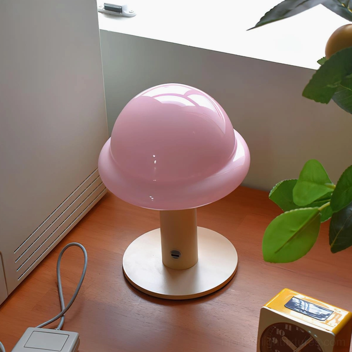 Pastel pink glossy mushroom cordless table lamp on wooden desk with green plant and light wood stand