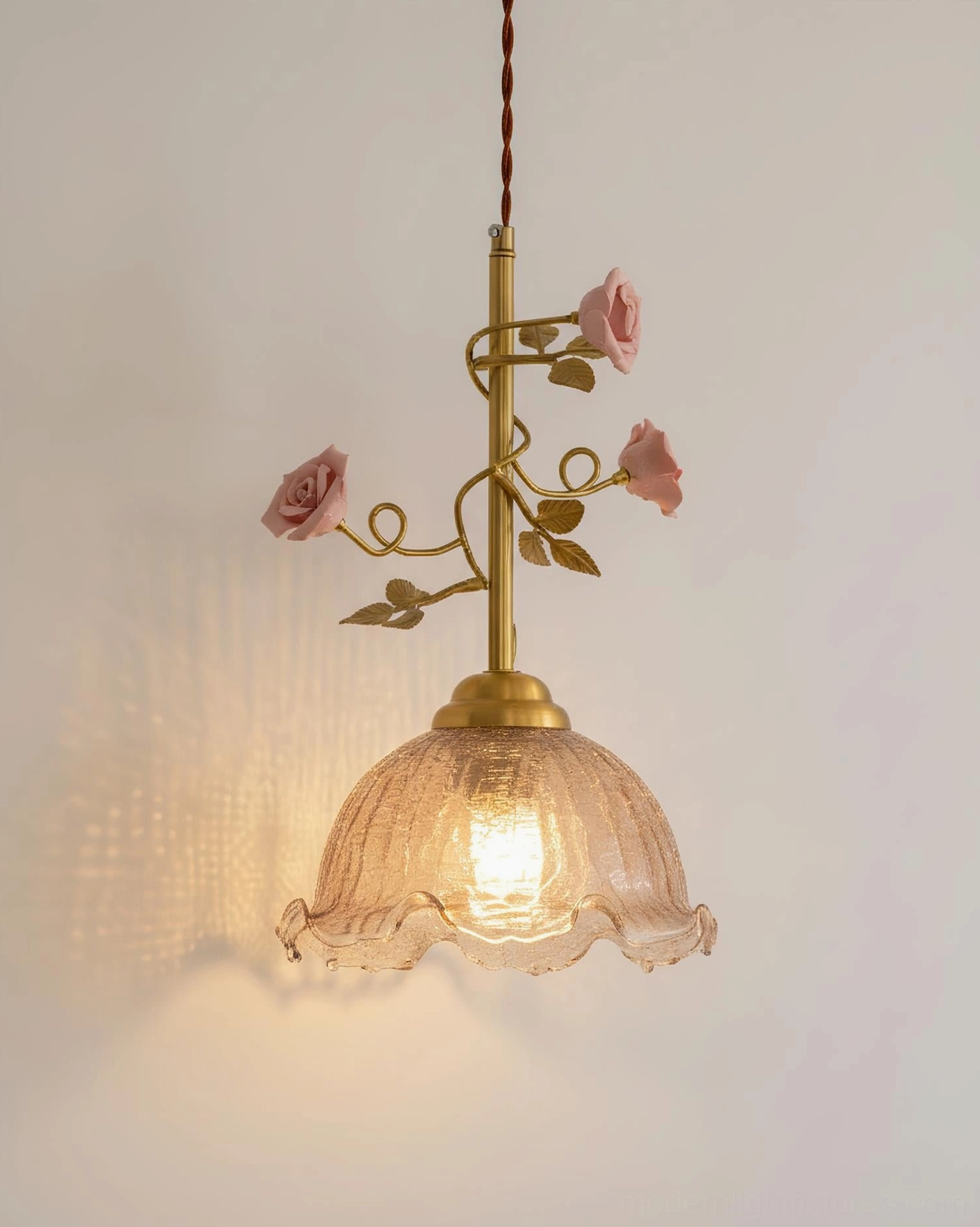 Lit Rosy Reverie pendant lamp with pink porcelain roses and brass gold frame against warm wall - cozy romantic vintage decor