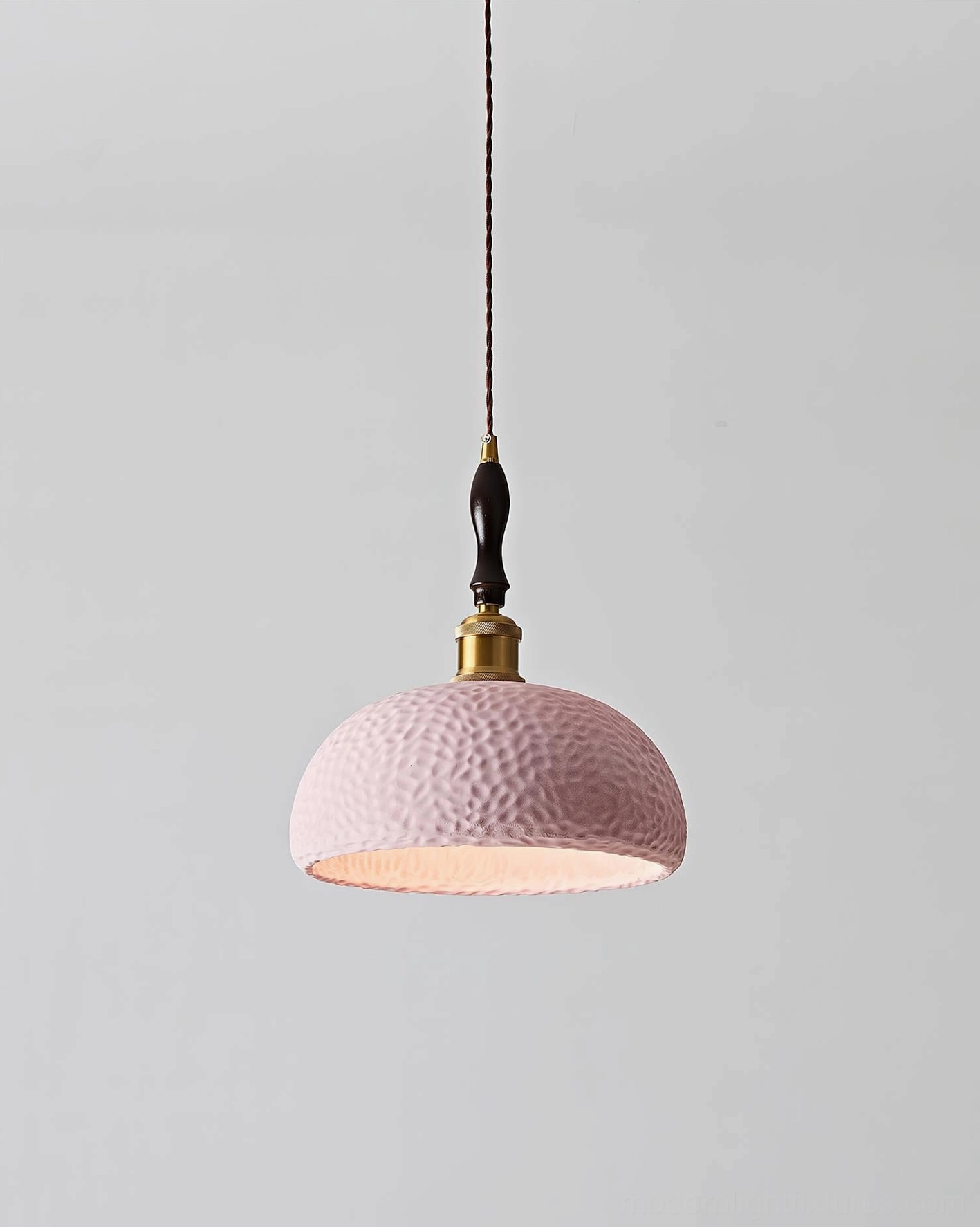 Soft pink textured resin dome pendant light hanging from brass hardware, front studio view