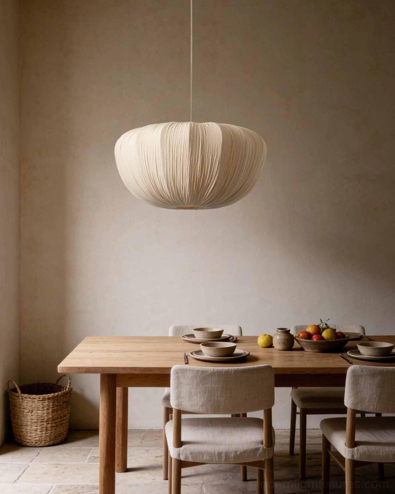 Beige pleated pendant lamp creating warm glow above dining table with wooden chairs and place settings