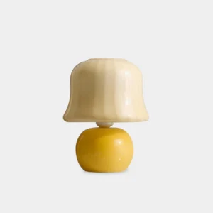 Handcrafted pleated mushroom table lamp with yellow ceramic base and ribbed milky glass shade in modern minimalist studio setting